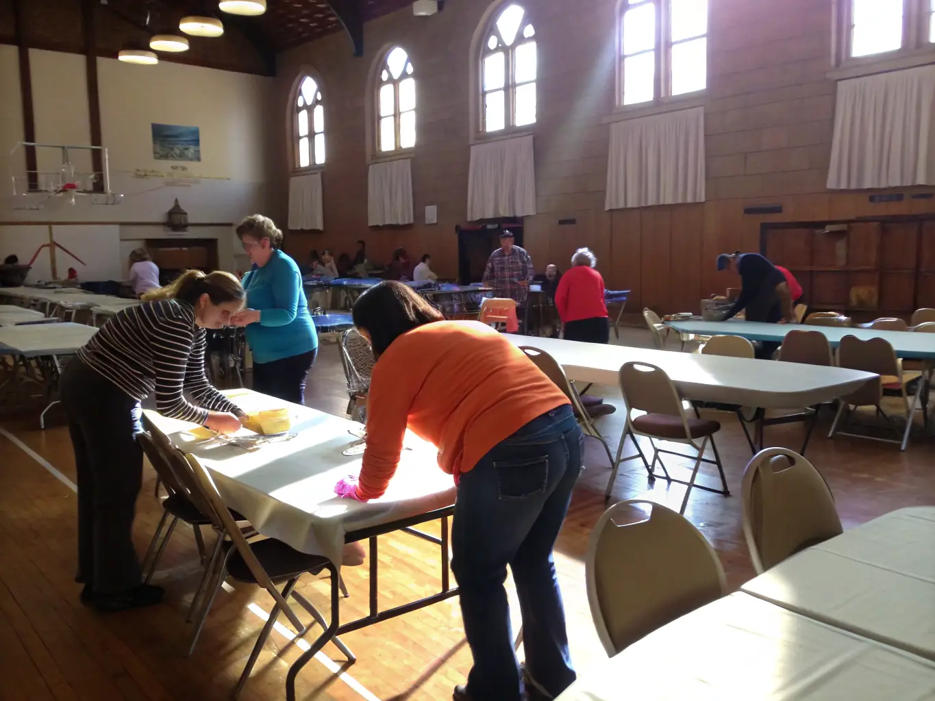 A diverse group of people volunteering at an ATELIER M event, smiling and engaged in various tasks such as setting up chairs, assisting with registration, and guiding attendees.